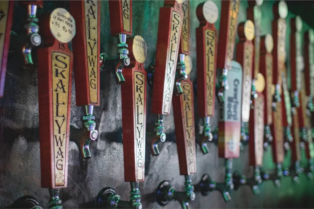 Close-up of numerous beer taps with brand names and prices.