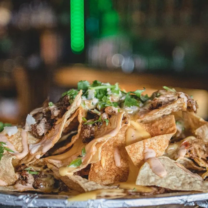 Close-up of a plate of loaded nachos with meat, cheese, and cilantro.