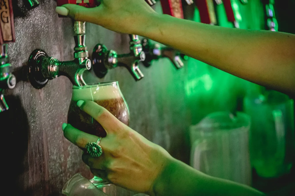 Hands pouring dark beer from a tap into a snifter glass.