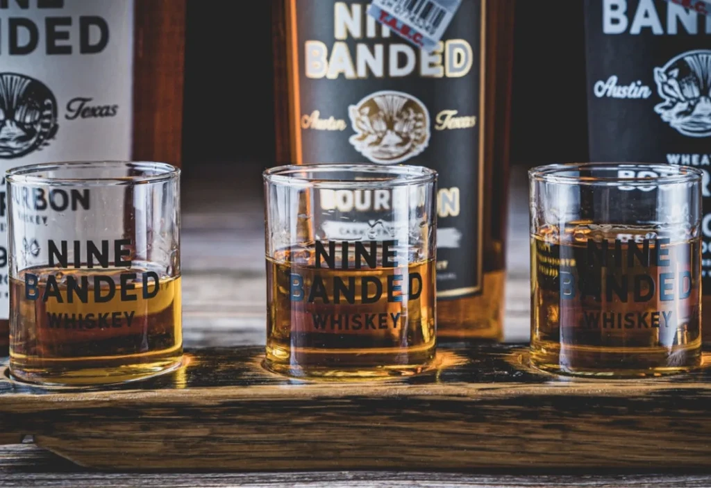 Nine Banded Whiskey in three glasses on a rustic wooden flight.