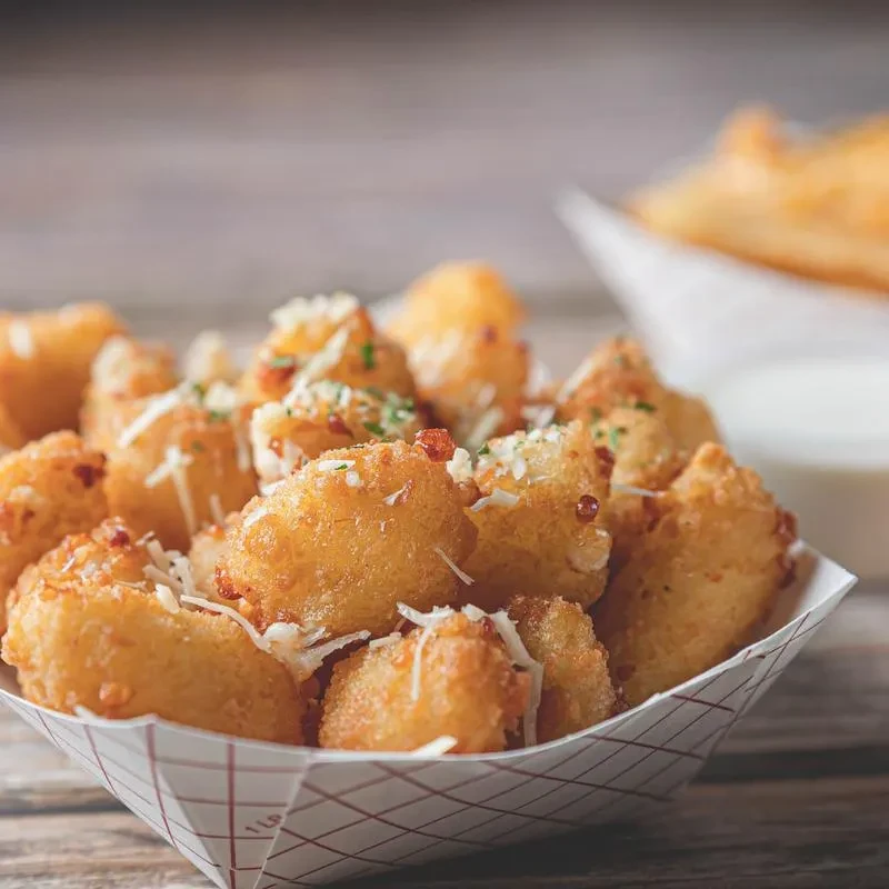 Crispy golden-brown fried items topped with cheese and herbs in a boat.