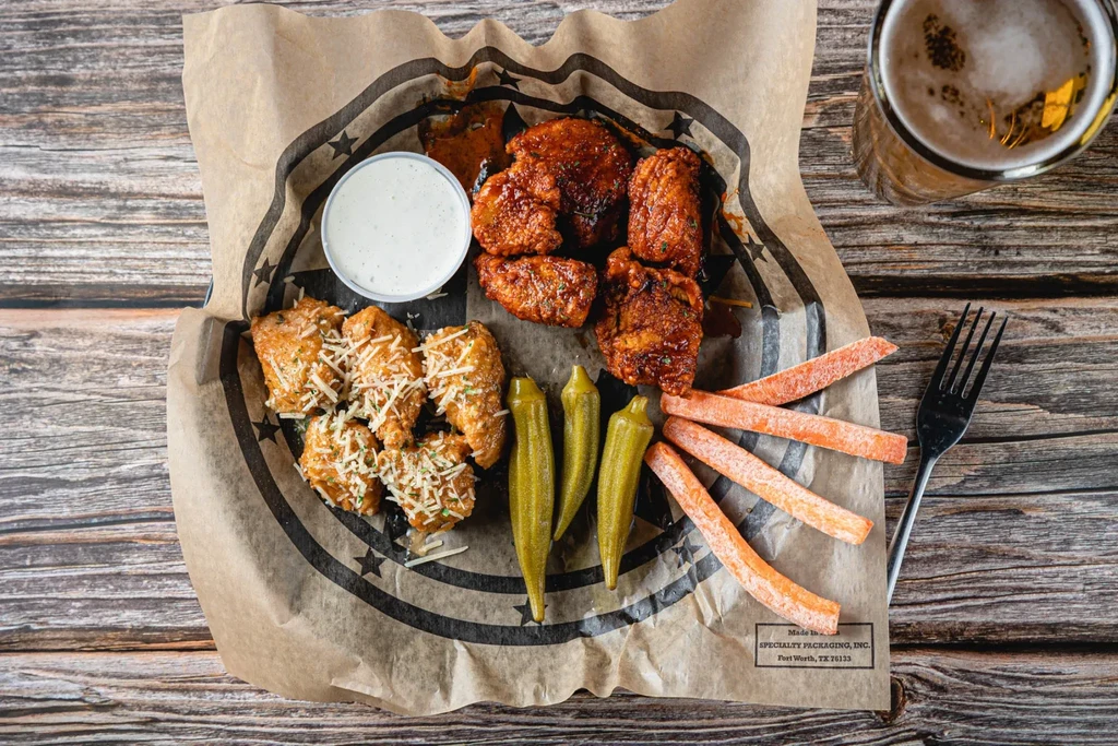 Overhead: Glazed and cheesy wings, veggies, dip, and beer on wooden table.