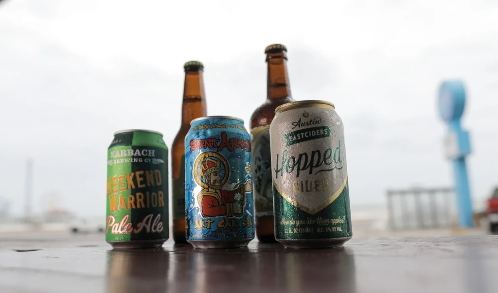 Four dewy cans and bottles of beer and cider on wood.