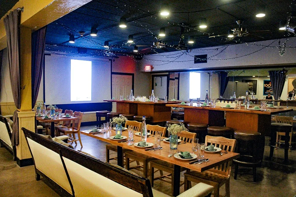 Dimly lit restaurant interior with set tables, industrial ceiling, and string lights.