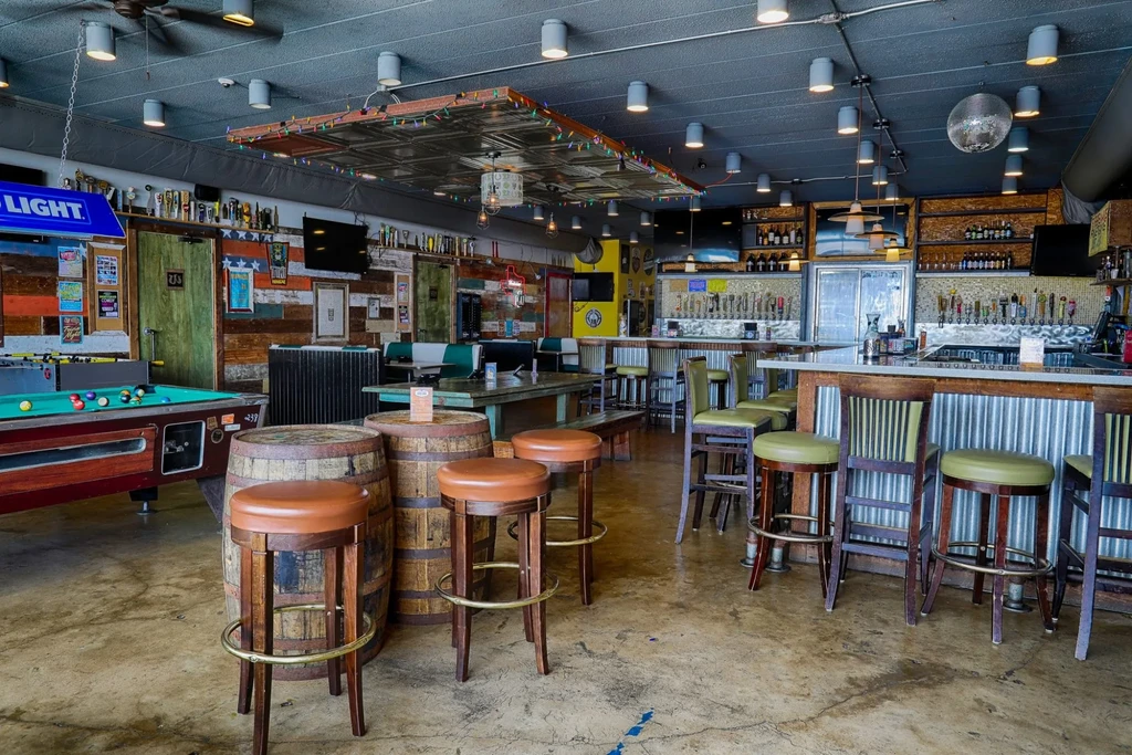 Casual bar interior with well-stocked bar, games, and barrel tables.