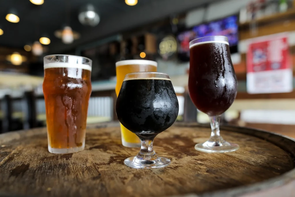 Four glasses of various beers on a dark wooden barrel.