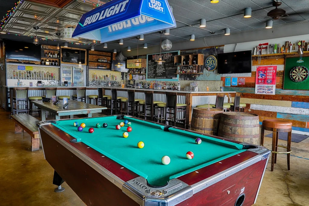 Empty bar interior featuring a pool table, long bar, and beer taps.