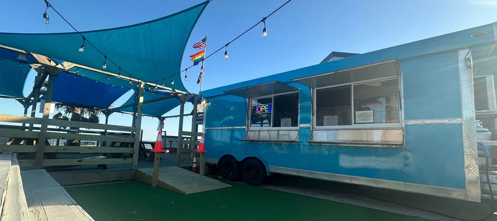 Blue food truck, outdoor dining deck with shade sails and flags.