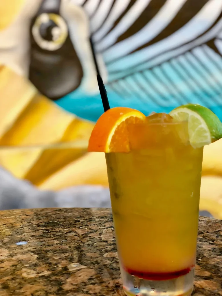 Vibrant yellow-orange cocktail with red bottom, orange, and lime slices.