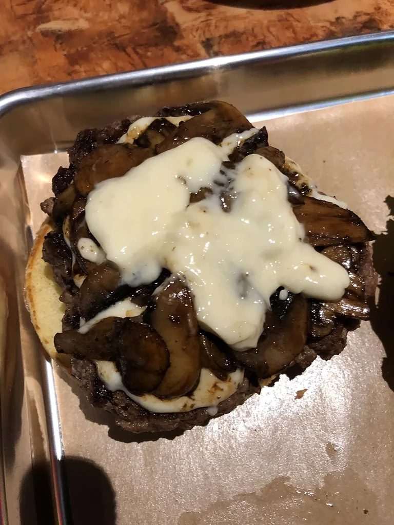 Open-faced burger with meat patty, sautéed mushrooms, and melted cheese.