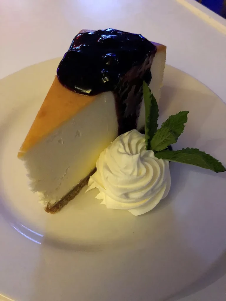 Cheesecake slice topped with dark fruit compote, whipped cream, and mint.