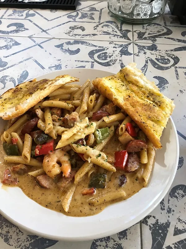 Close-up of penne pasta with shrimp, sausage, bell peppers, and garlic bread.