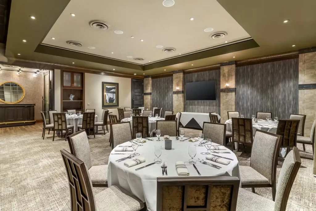 Well-appointed, empty restaurant dining room with multiple set round tables.