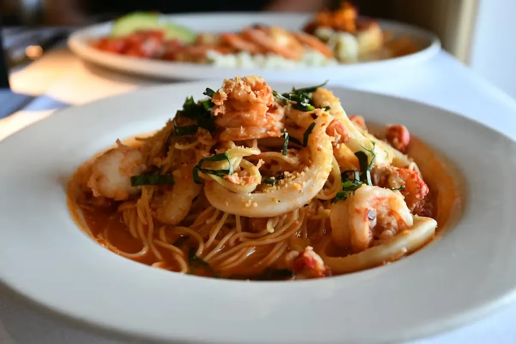Reddish-orange seafood pasta with shrimp, calamari, green herbs.