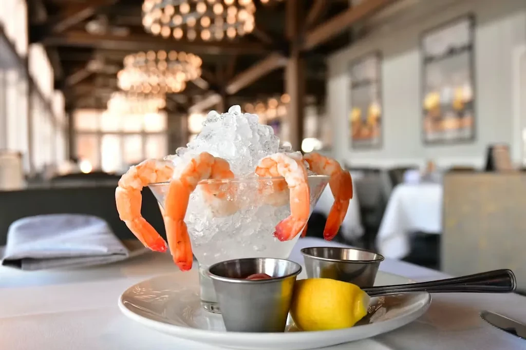 Cooked shrimp cocktail in martini glass with lemon, sauce, restaurant background.