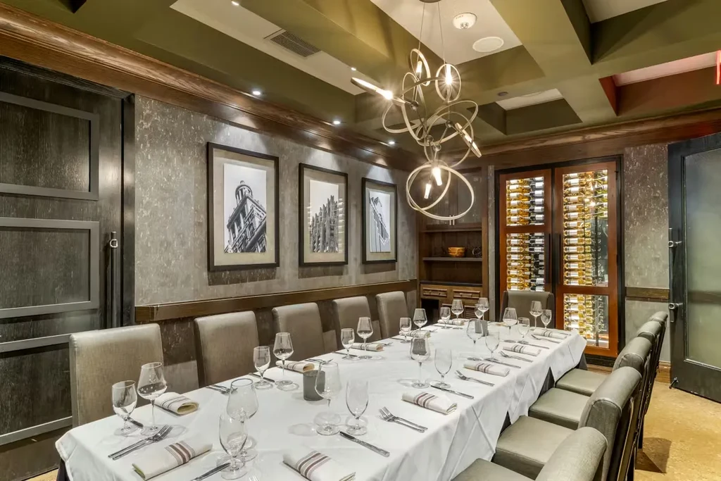 Modern private dining room with set table, chandelier, and glass wine cellar.