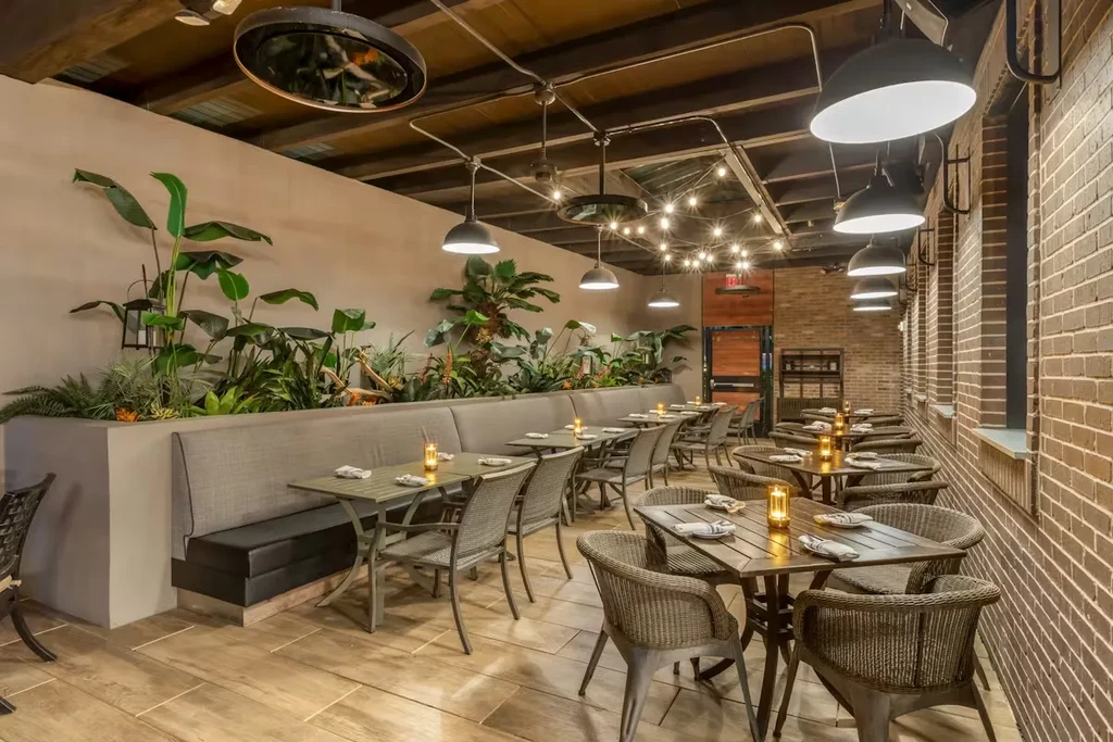 Contemporary restaurant interior with banquettes, brick wall, and plants.