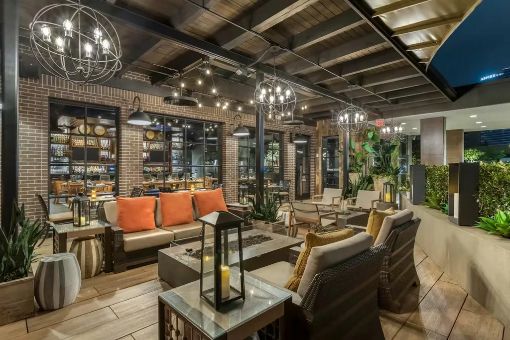 Elegant outdoor lounge with warm lighting, brick, wood, and green plants.