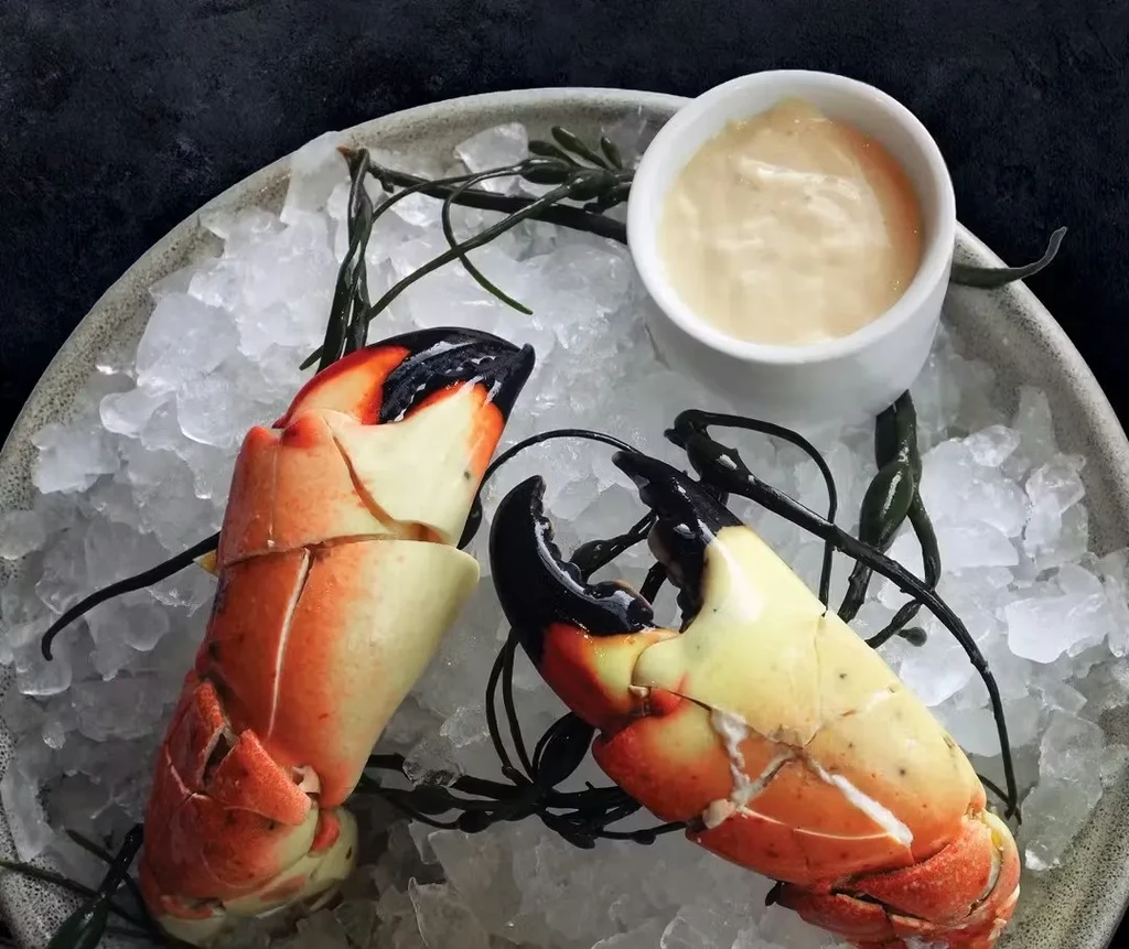 Two cooked crab claws on ice with green garnish and dipping sauce.