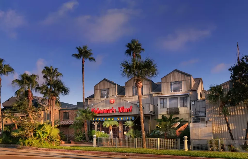 Multi-story Fisherman's Wharf Seafood Grill building with metal siding and palms.