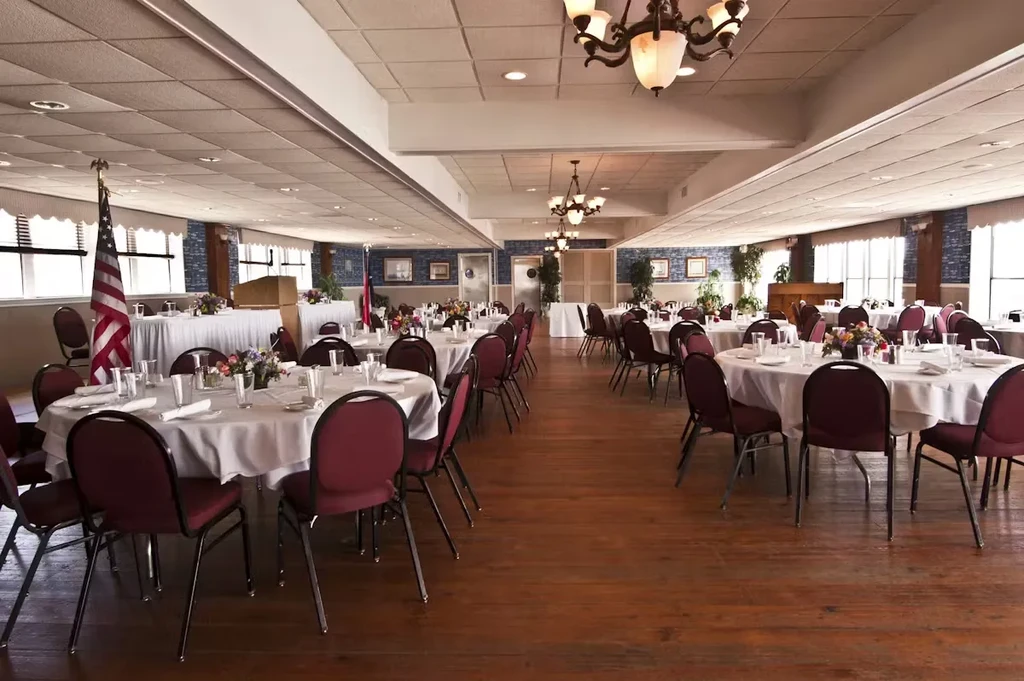 Empty banquet hall with round tables, maroon chairs, and an American flag.