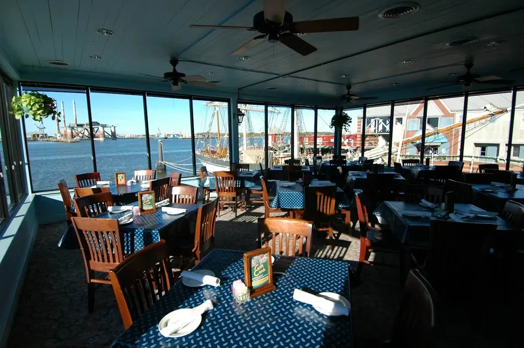 Empty waterfront restaurant dining room with harbor view and blue tables.