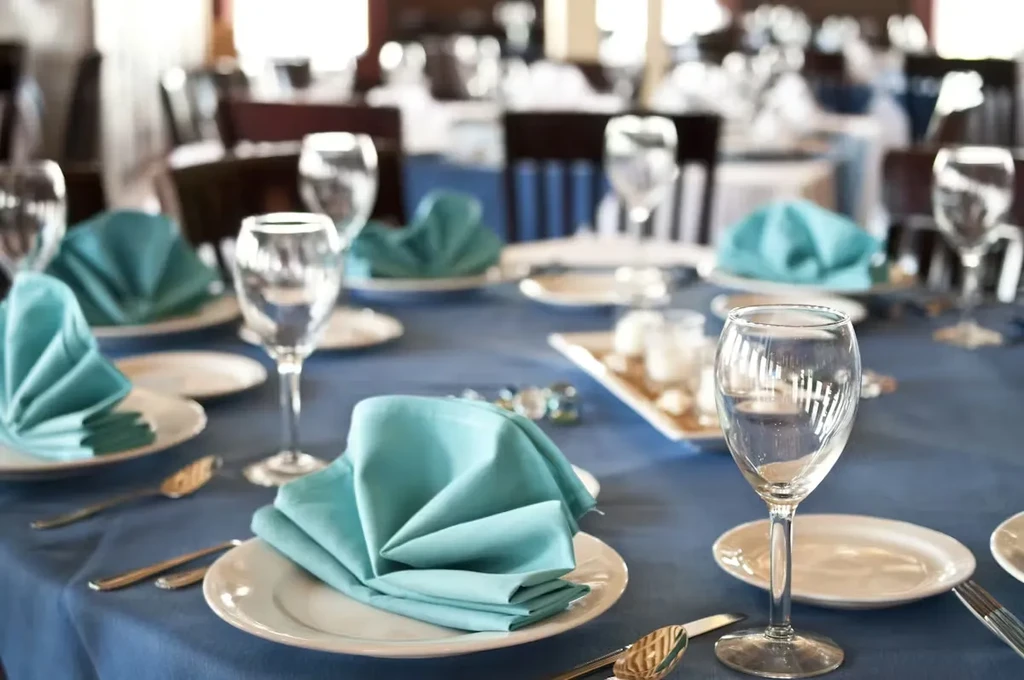 Restaurant table with royal blue cloth, white plates, turquoise napkins.