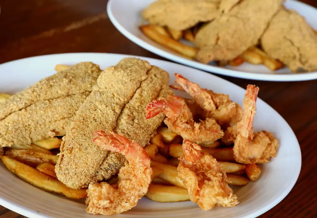 Two plates of golden fried fish, shrimp, and fries.