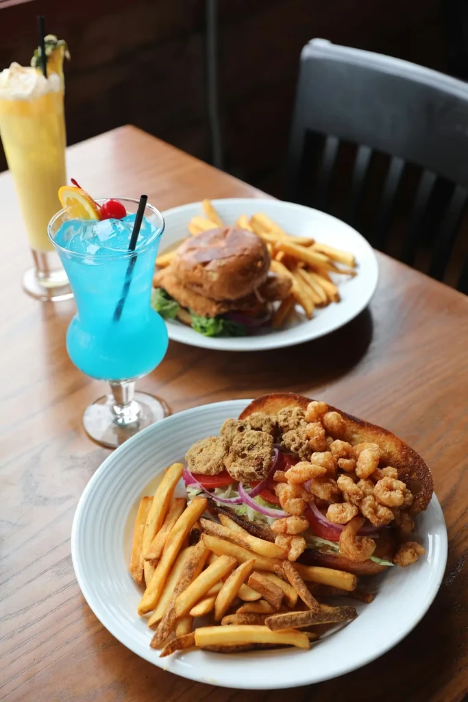 Fried shrimp po'boy, french fries, and blue cocktail on a wooden table.