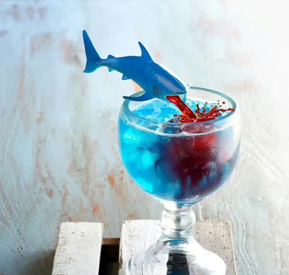 Blue cocktail in goblet, a shark pouring red syrup.