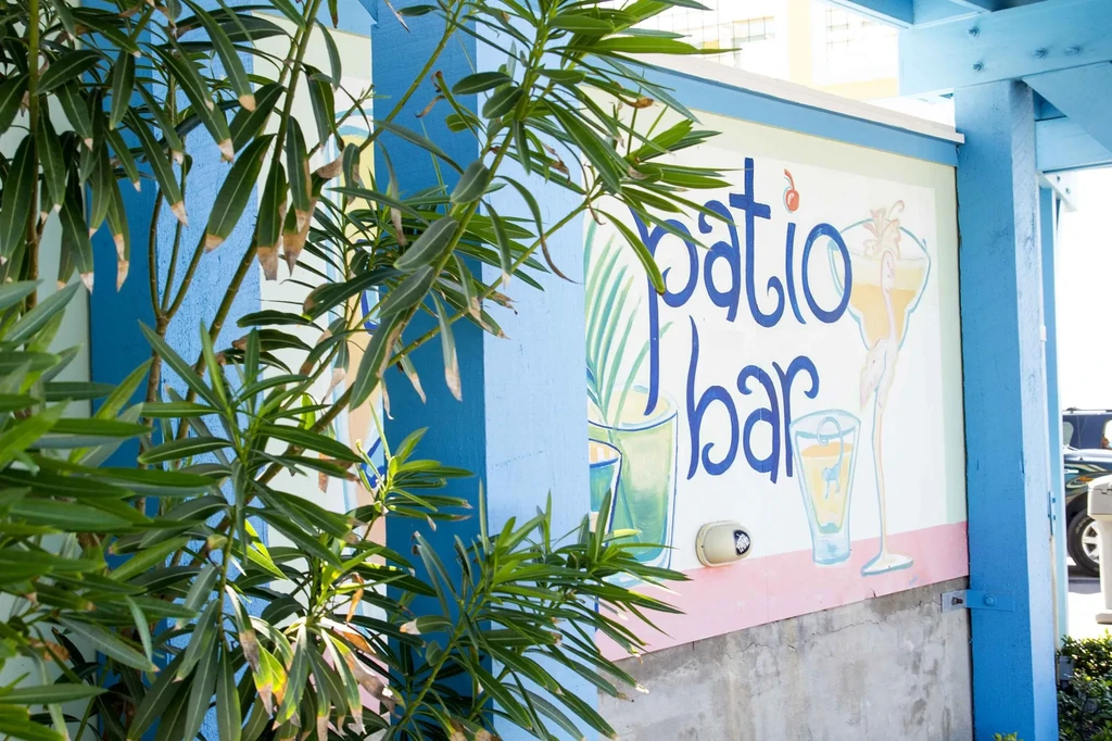 Exterior mural 'patio bar' with cocktails, framed by pillars and foliage.