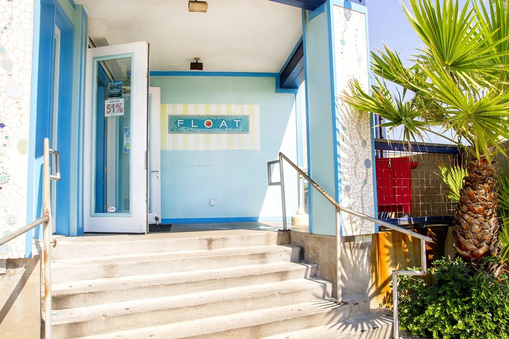 Blue mosaic-tiled 'FLOAT' entrance with a sunny staircase and palm tree.