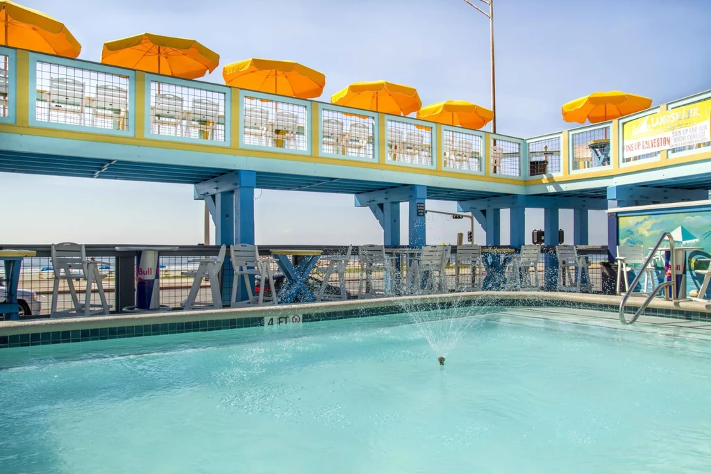 Colorful multi-level outdoor restaurant with pool, ocean, bikini contest sign.