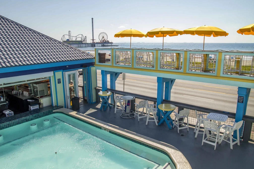 Sunny beachfront restaurant with pool, patio, ocean, and pier amusement rides.