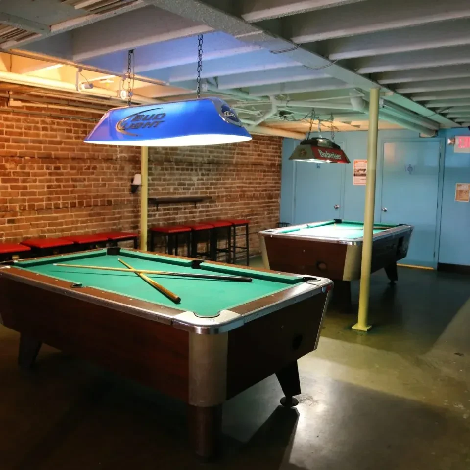 Two pool tables with Bud Light and Budweiser lights in a bar.