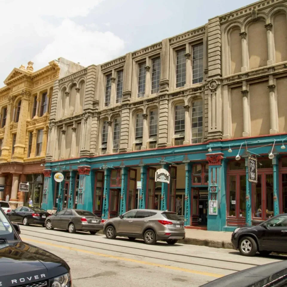 Urban street with classical buildings, colorful ground floors, vehicles, and tracks.