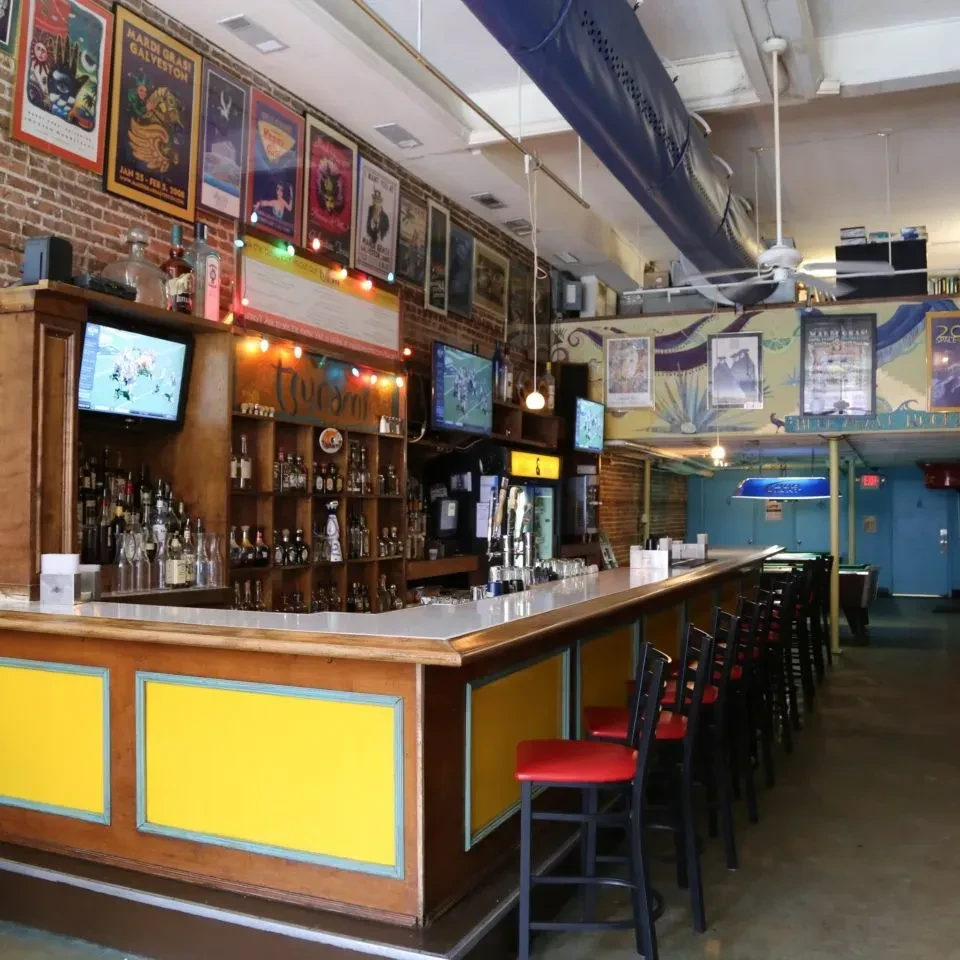Festive, empty bar with a yellow counter, beer taps, and pool table.