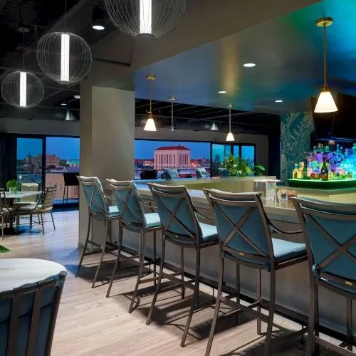 Empty modern bar with teal stools, liquor bottles, and city view.