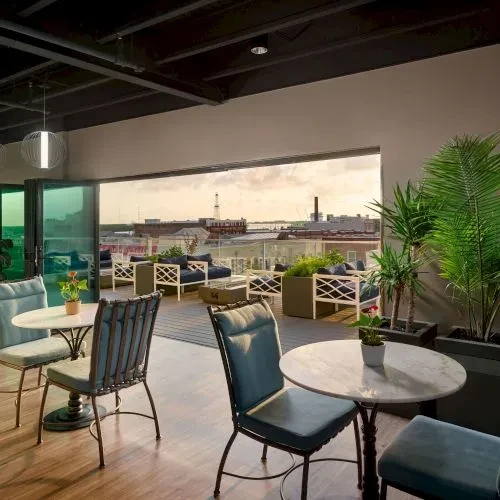 Chic rooftop restaurant terrace with city view, blue chairs, and plants.