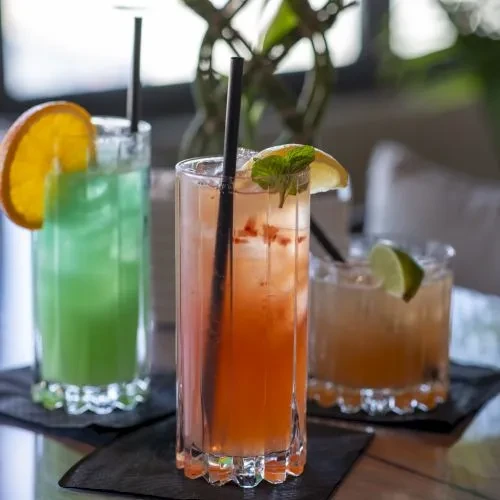 Three cocktails: orange, green, amber, garnished in fluted glasses.