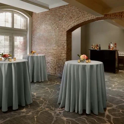 Elegant interior with three candlelit cocktail tables, florals, and brick wall.