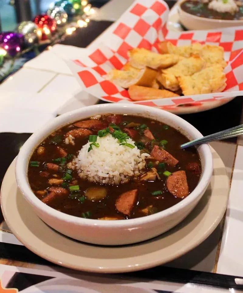 Bowl of dark gumbo with rice, sausage, and green onions.
