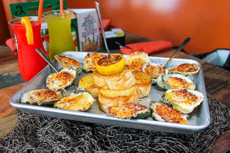 Golden-brown baked oysters, bread, grilled lemon, and two colorful cocktails.