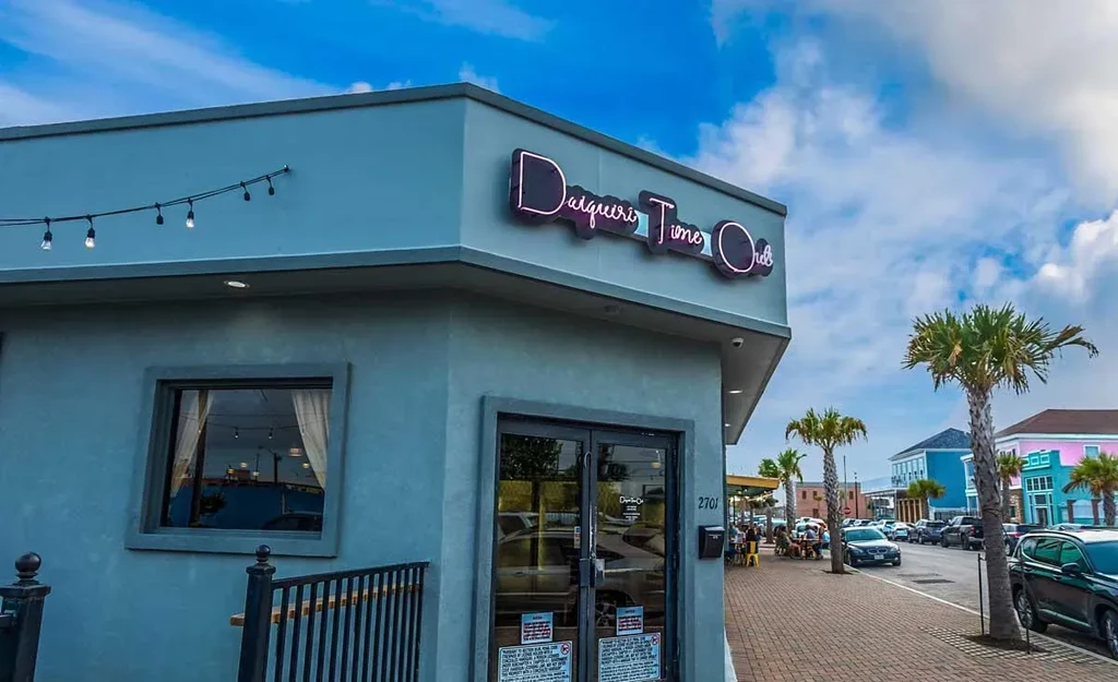 Modern 'Daiquiri Time Out' building, neon sign, palm trees, blue sky.