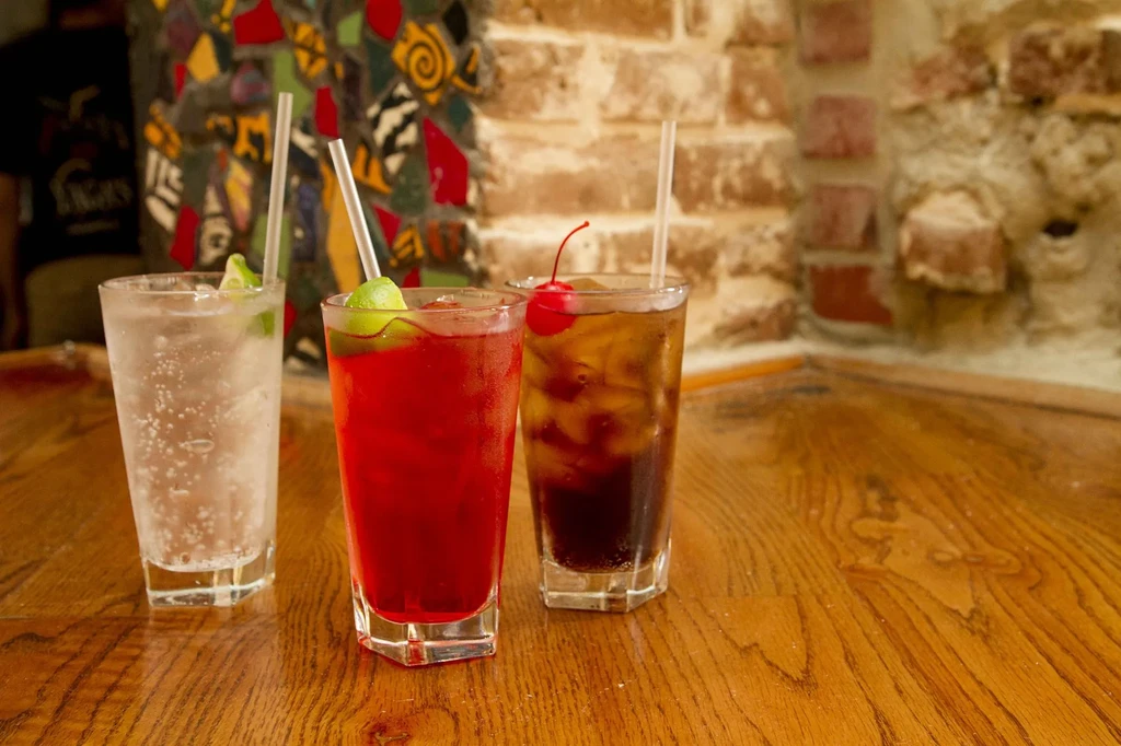 Three faceted drinks: clear, red, and amber, with lime and cherry.