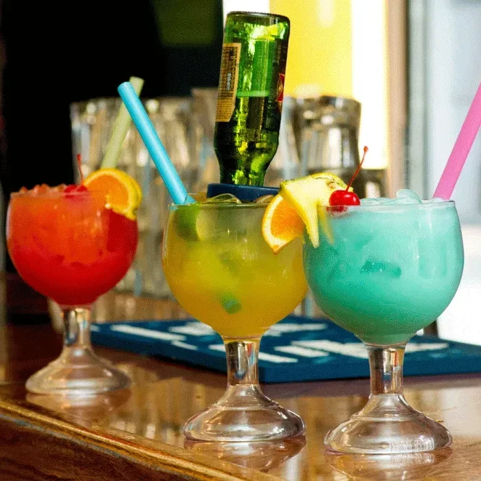 Three colorful hurricane cocktails, one with an inverted green beer bottle.