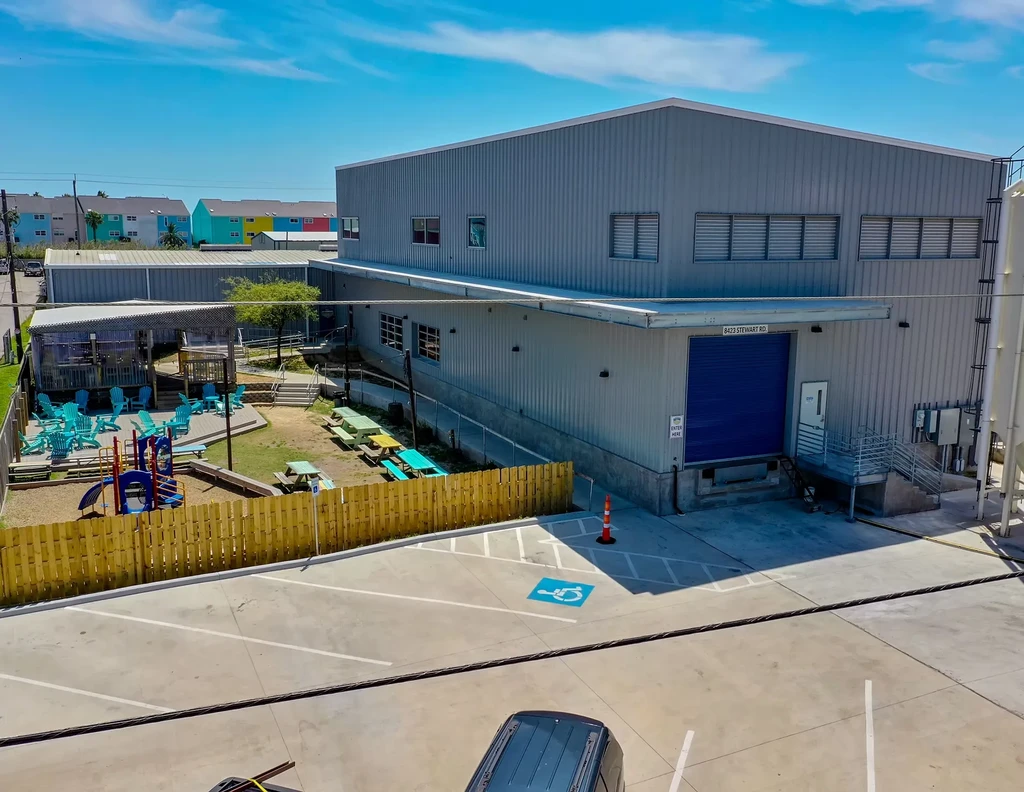 Aerial view of industrial building, parking, playground, and outdoor seating.
