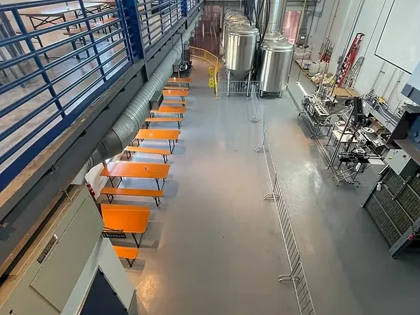 Overhead view: spacious brewery with orange tables, tanks, production line.