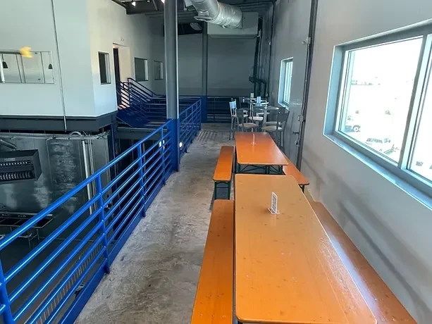 Empty industrial brewery mezzanine with picnic tables overlooking tanks.