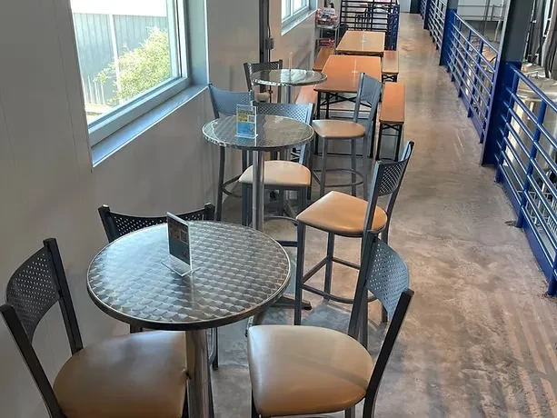 Modern industrial bar with high-top tables, blue railing, brewery tanks.